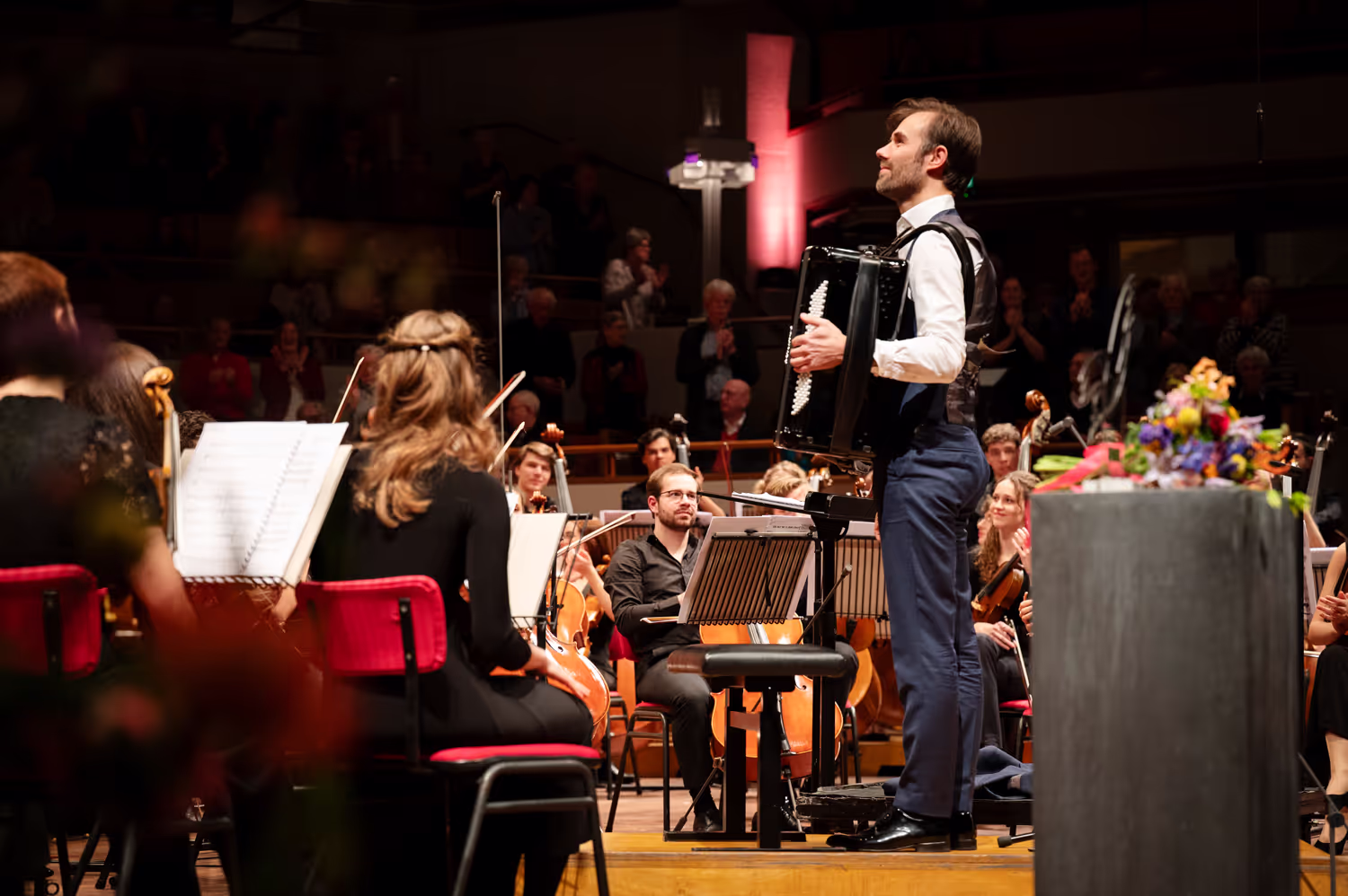 Concertfoto van een accordeonist omringd door een orkest.